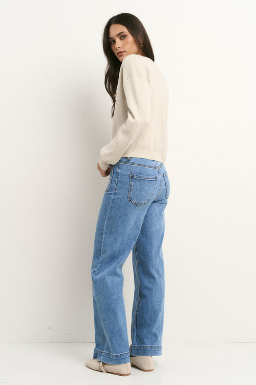 Woman wearing blue jeans and a white sweater against a white background
