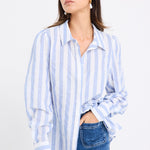 Woman wearing a relaxed blue and white vertical stripe shirt with balloon sleeves, styled casually with wide-leg blue jeans.







