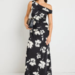 Woman wearing a one-shoulder black floral maxi dress, styled with black heels and a clutch for an elegant evening look.