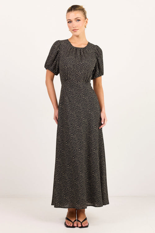 A woman modeling a short-sleeved midi dress with a black and white abstract pattern, standing against a plain white studio background.
