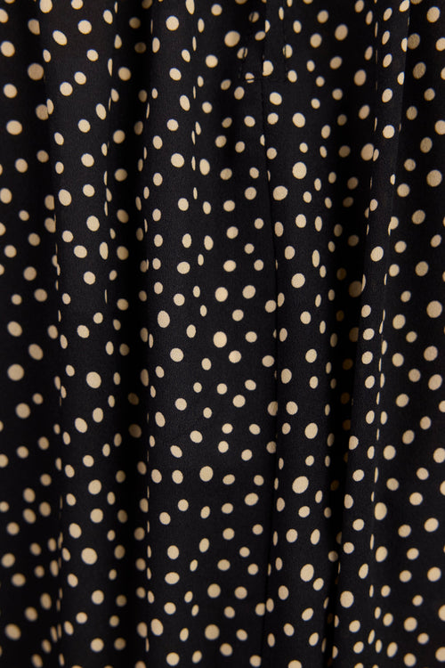 Close-up of a black fabric with a repeating beige polka dot pattern.