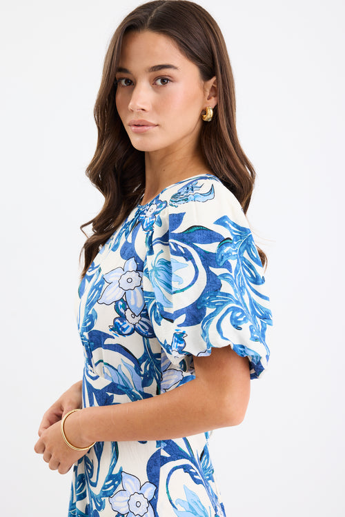 A short-sleeve floral dress with puff sleeves and a bias-cut design. The dress features a blue floral print on a cream background and is fully lined for comfort.