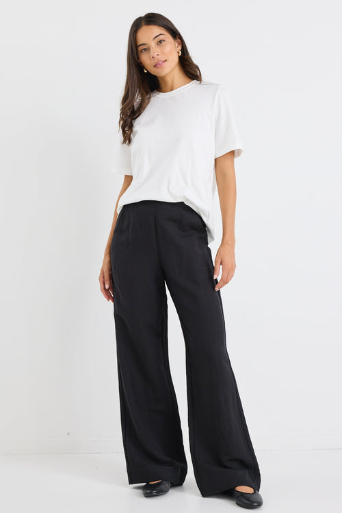 Woman wearing a relaxed-fit ivory short sleeve tee tucked into high-waisted black trousers, styled with minimal makeup and gold earrings.







