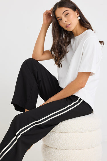 Woman wearing black wide-leg pants with white side stripes, featuring a mid-rise elastic waistband and paired with sneakers.