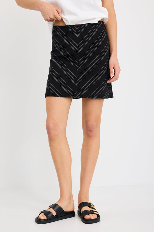 Woman wearing a black and white gradient stripe mini skirt in a chevron pattern, styled with a simple white tee and black sandals.