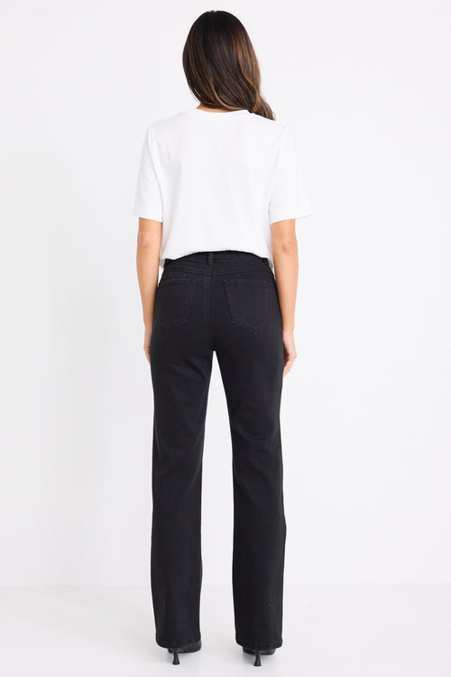 Woman wearing mid-rise, black wash jeans with a plain beige t-shirt and nude sandals.