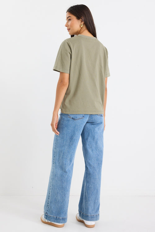 model wears a green khaki t-shirt with light blue jeans
