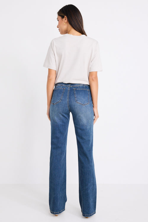 Woman wearing mid-rise, mid blue wash jeans with a plain beige t-shirt and nude sandals.