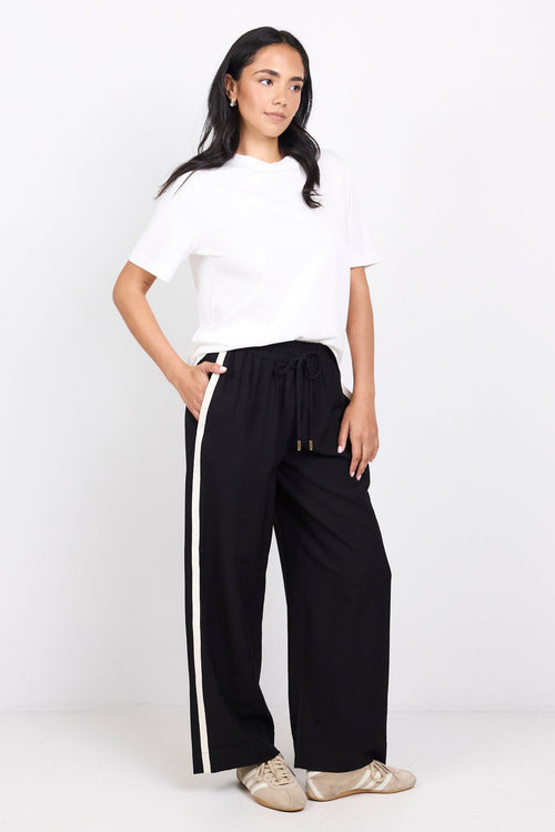 Woman wearing a white top and black pants with white stripes on a white background