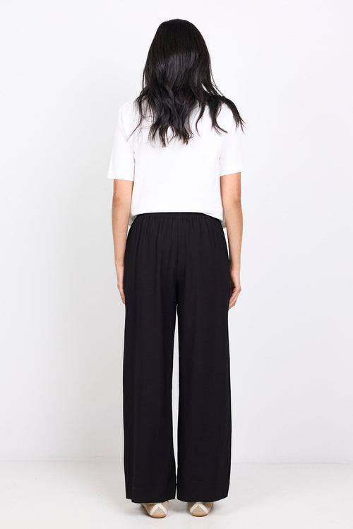 Person wearing a white top and black pants on a white background