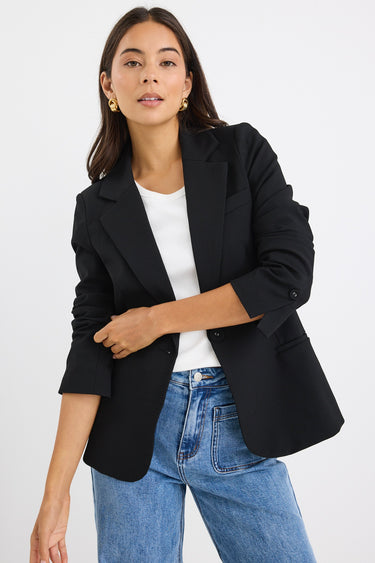 model wears a black fitted blazer and blue wide leg jean