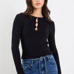 Woman wearing a black long-sleeve top with a unique neckline and blue jeans on a white background