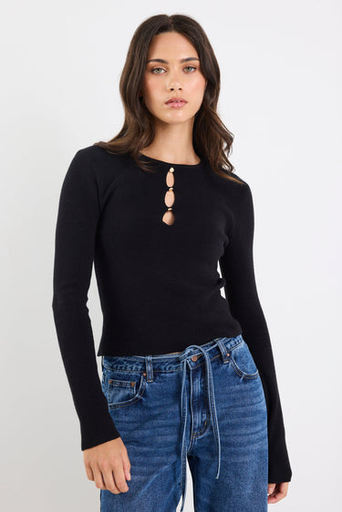 Woman wearing a black long-sleeve top with a unique neckline and blue jeans on a white background