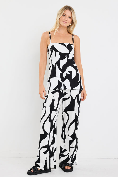 Woman wearing a sleeveless black and white abstract print top with a square neckline and fitted waist, styled with loose blonde hair and gold hoop earrings.