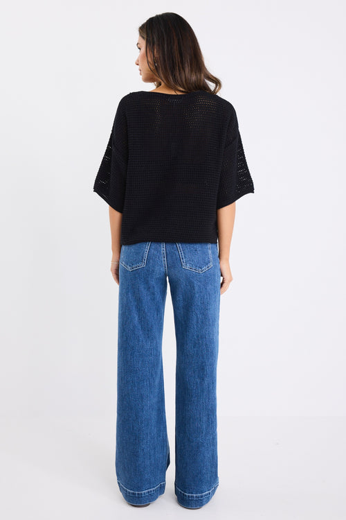 our model wears a black crochet knit top with mid blue jeans