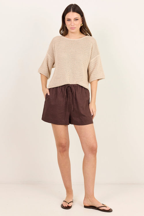 A woman modeling a beige textured knit short-sleeve top and dark brown drawstring shorts against a plain off-white studio background.