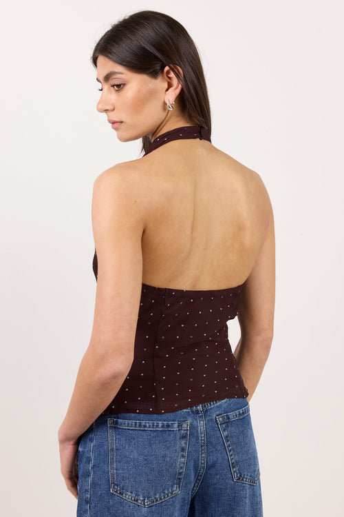 A woman shown from the back wearing a dark brown halter top with small white polka dots and blue jeans, photographed against a plain light background.