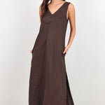 A woman modeling a sleeveless, V-neck maxi dress in a dark brown color, standing against a plain white studio background.