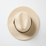 Taupe woven Panama-style hat with a brown band and gold buckle detail, photographed on a white background