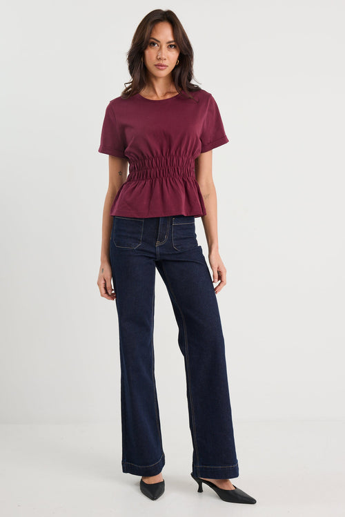 Woman wearing a burgundy top and dark blue jeans on a white background