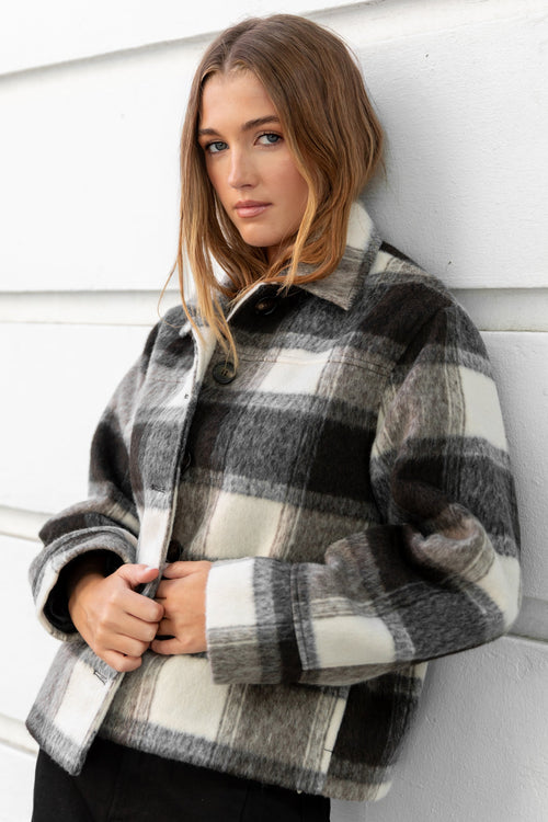 Woman wearing a plaid jacket against a white wall