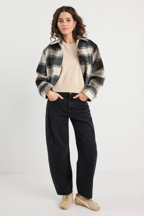 Person wearing a plaid shirt, beige sweater, black pants, and beige shoes on a white background