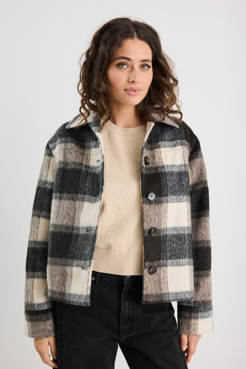 Woman wearing a plaid jacket over a beige sweater on a white background
