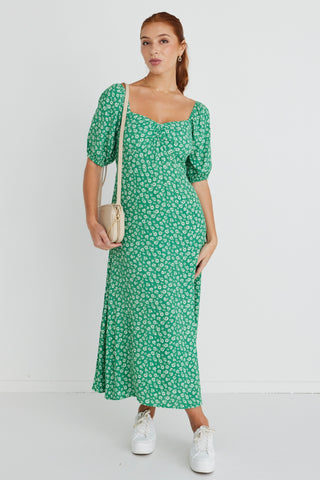 Model wears a green floral print maxi dress with white sneakers and a beige handbag.  