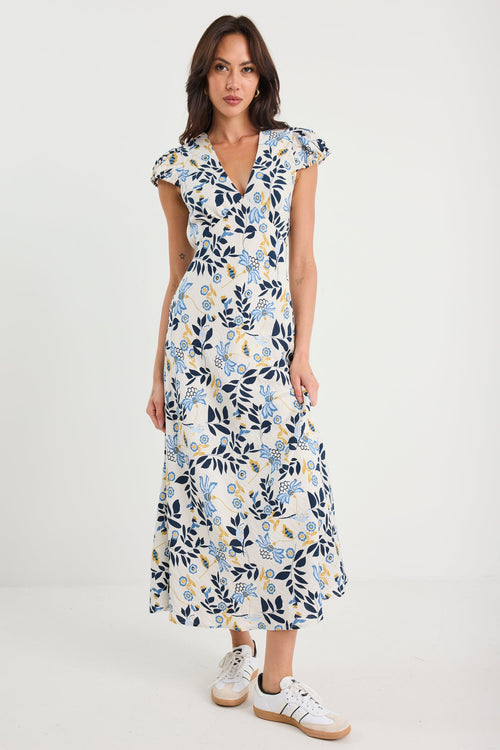 Woman wearing a floral dress with white sneakers on a plain background