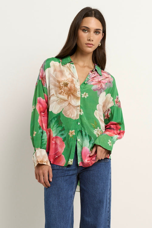 Woman wearing a green oversized button-up shirt with large floral print in pink, white, and beige tones.