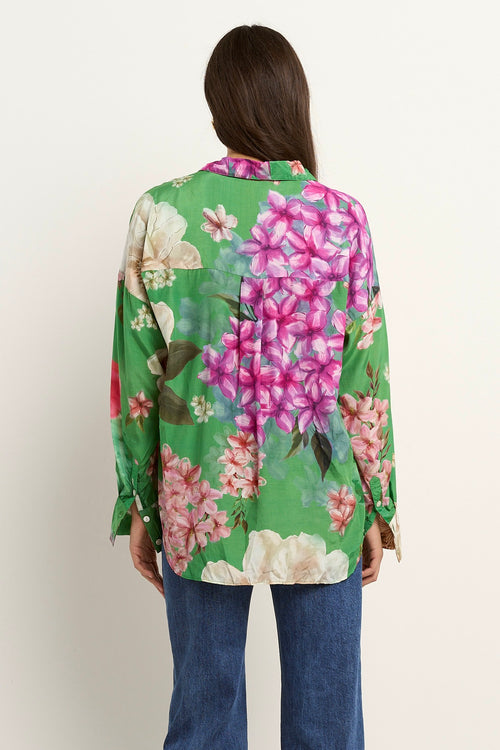Woman wearing a green oversized button-up shirt with large floral print in pink, white, and beige tones.