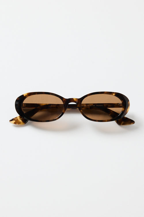 Narrow tortoiseshell oval sunglasses with warm brown tinted lenses, photographed against a white background