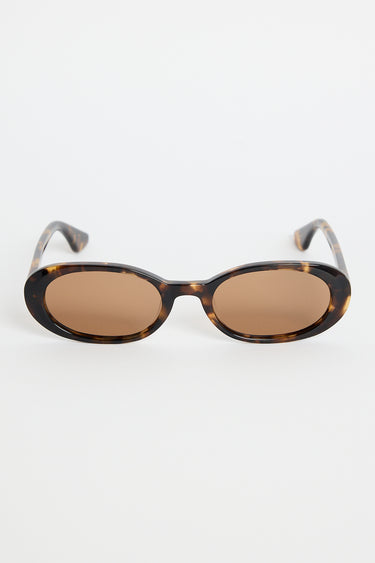 Narrow tortoiseshell oval sunglasses with warm brown tinted lenses, photographed against a white background