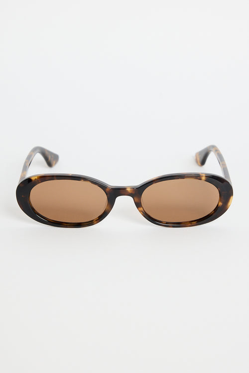 Narrow tortoiseshell oval sunglasses with warm brown tinted lenses, photographed against a white background