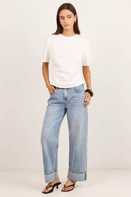 A woman modeling a white short-sleeve t-shirt and light-wash wide-leg blue jeans with rolled cuffs, paired with black sandals, against a plain off-white studio background.