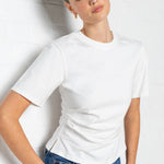 Woman wearing a white t-shirt with side ruching and blue jeans against a plain background