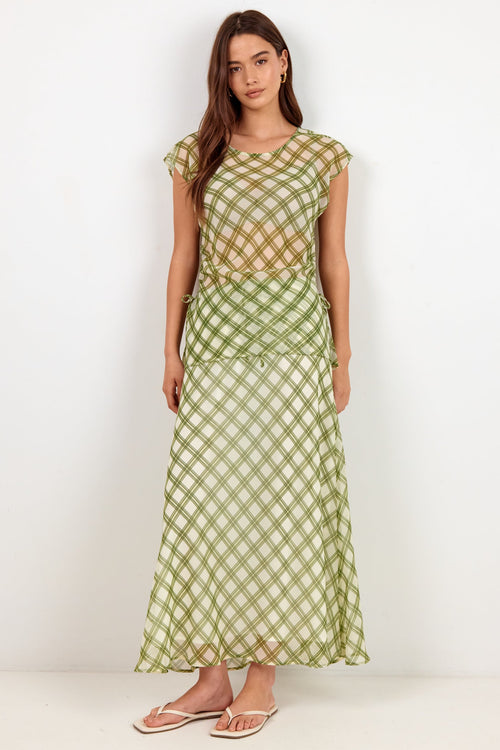 A woman modeling a light green and white gingham check maxi dress with a sheer mesh overlay on the bodice, standing against a plain white studio background.
