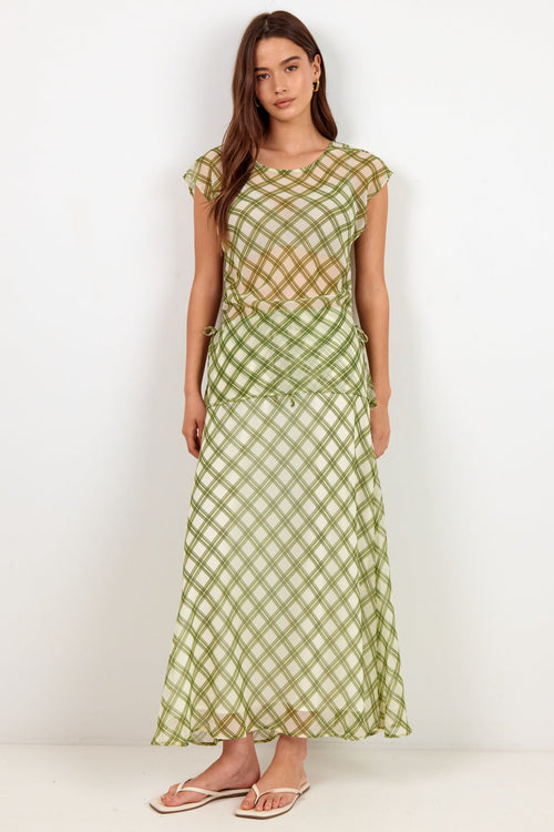 A woman modeling a light green and white gingham check maxi dress with a sheer mesh overlay on the bodice, standing against a plain white studio background.
