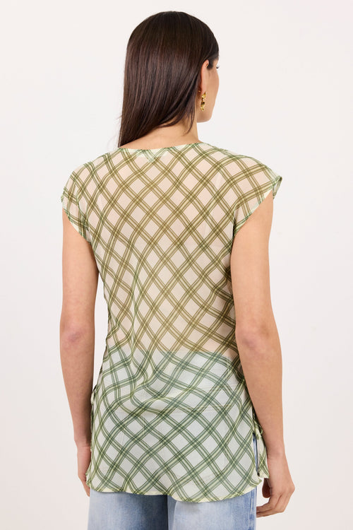 A woman viewed from the back wearing a short-sleeve top with a green and beige plaid pattern and light blue jeans, against a plain white background.