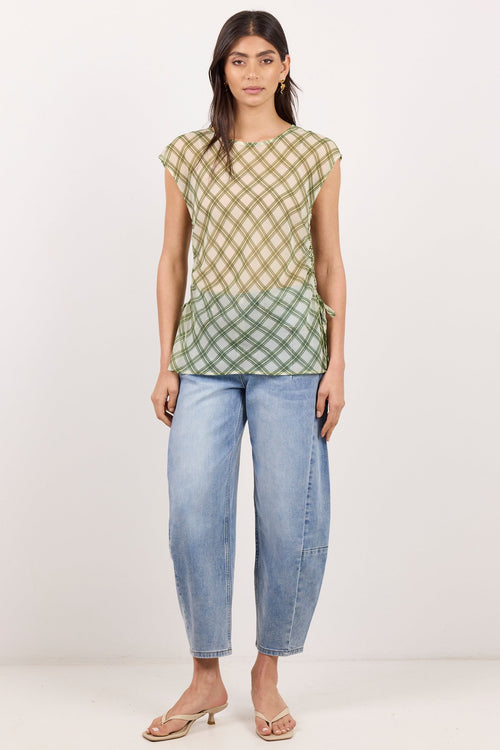 A woman modeling a short-sleeve top with a beige and green gingham pattern and a gradient transition at the hem, paired with light-wash blue jeans and beige sandals, against a plain white studio background.