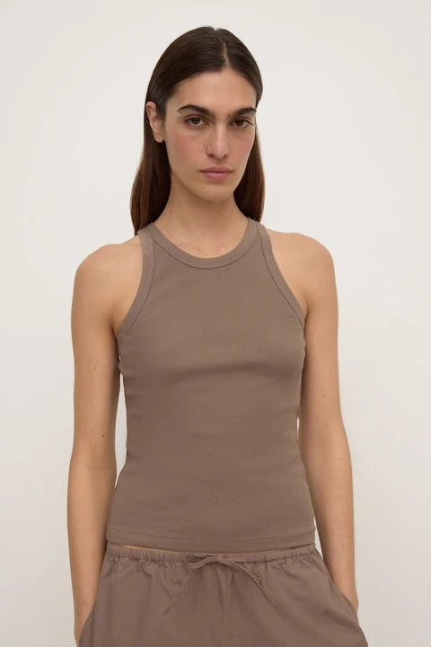 A woman modeling a sleeveless ribbed tank top in a muted taupe-brown color, paired with matching drawstring bottoms, against a plain off-white studio background.
