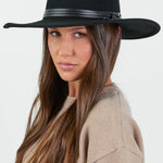 A stylish black Panama wool hat with a wide brim and a sleek black stacked trim band, set against a neutral background. The hat has a structured design and a minimalist aesthetic, adding an elegant touch to any outfit.