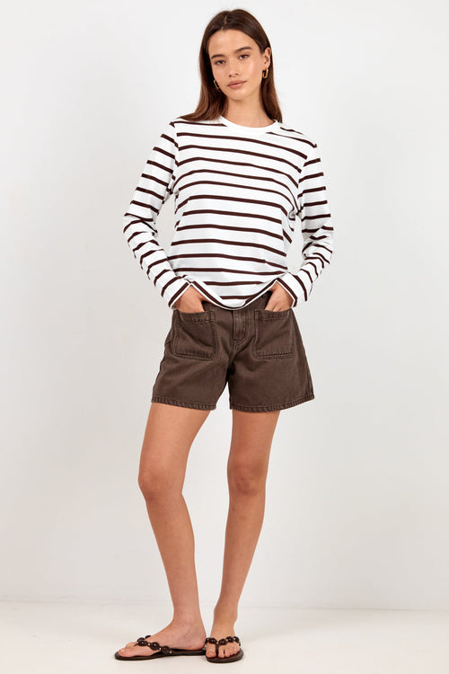 A woman modeling a long-sleeve black and white striped knit top paired with dark brown shorts and black sandals, standing against a plain white studio background.
