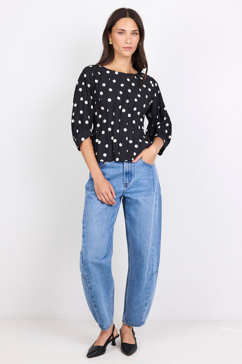 Woman wearing a black polka dot blouse and blue jeans on a white background