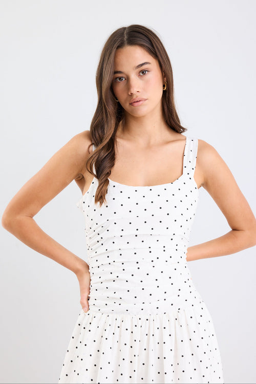 Woman wearing a white polka dot dress against a plain background