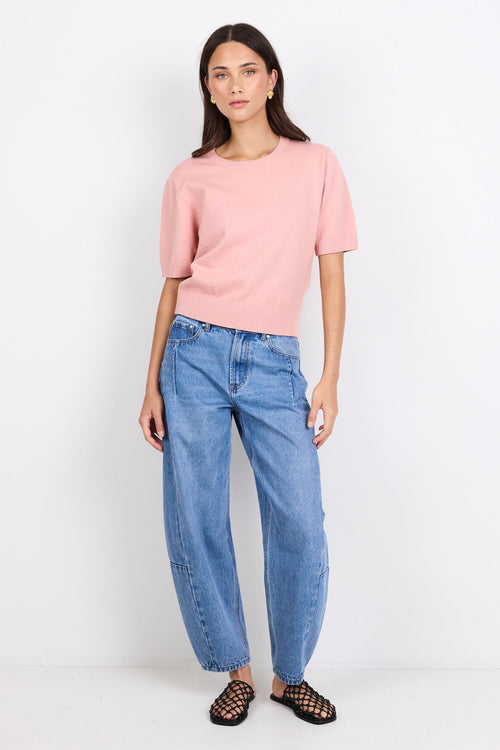 Woman wearing a pink sweater and blue jeans on a white background