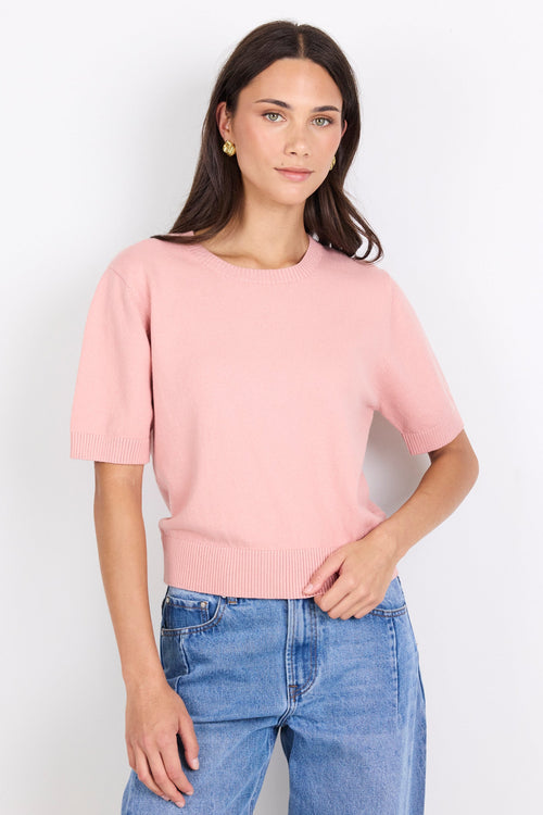 Woman wearing a pink sweater and blue jeans against a white background