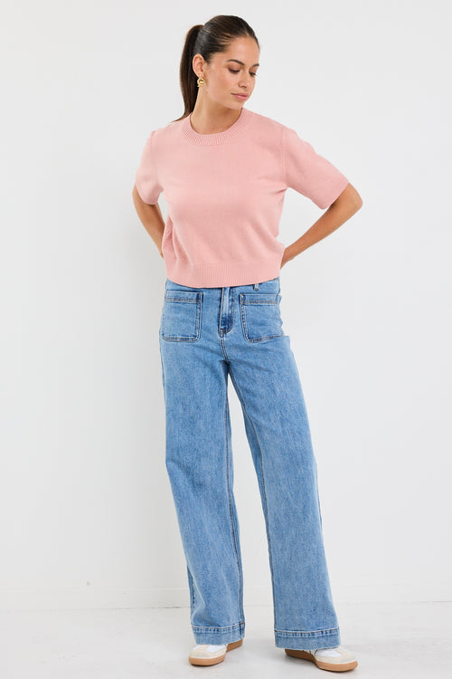 Woman wearing a blush pink short sleeve knit top with crew neckline and light blue high-waisted jeans.