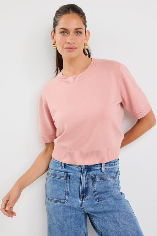 Woman wearing a blush pink short sleeve knit top with crew neckline and light blue high-waisted jeans.