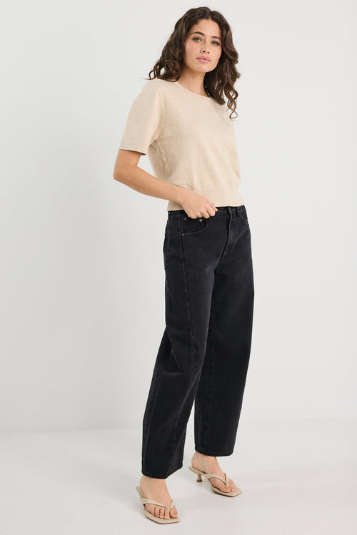 Woman wearing a beige top and black pants on a white background